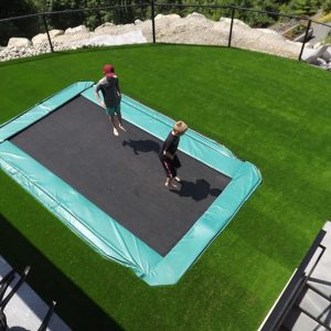 children playing on trampoline submerged within artificial grass lawn backyard