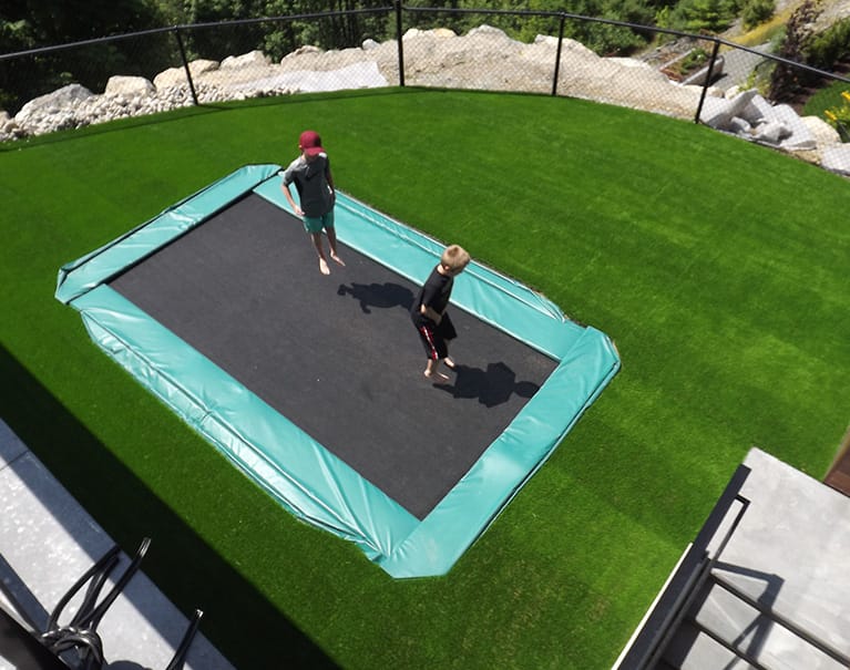 children playing on trampoline submerged within artificial grass lawn backyard