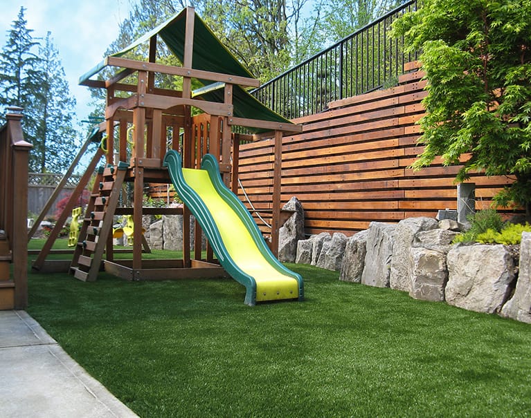 wooden playground structure with slide atop artificial grass lawn