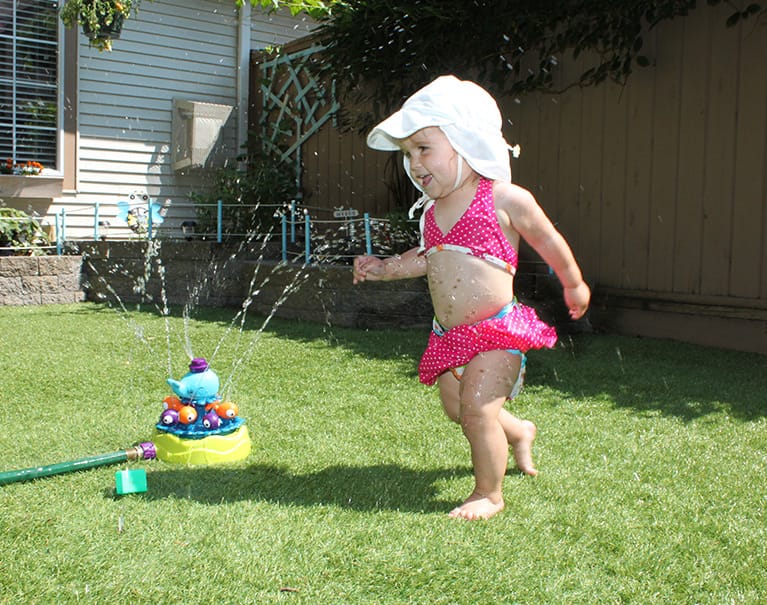 child playing in the sprinkler on artificial grass backyard lawn