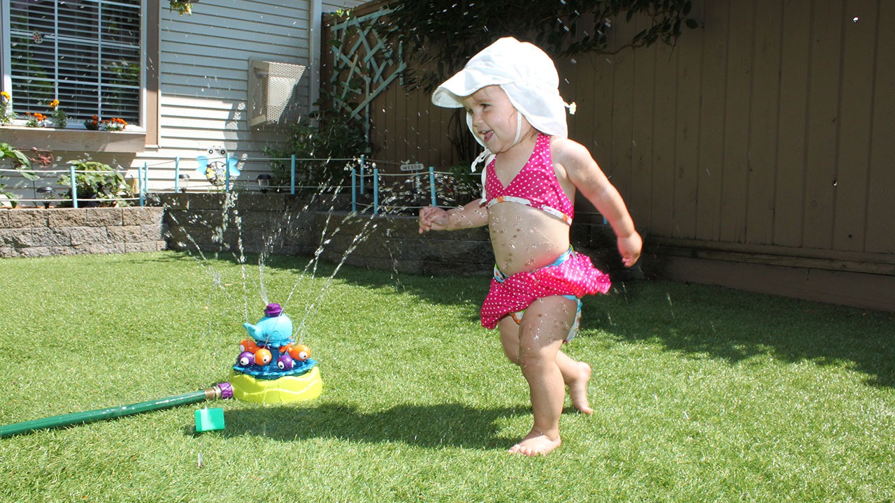 child playing in the sprinkler running on artificial grass