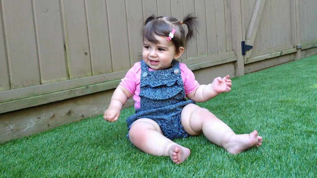 child sitting on artificial grass in backyard 