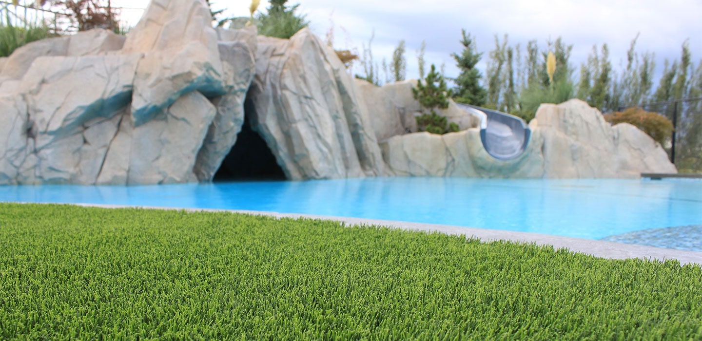 artificial grass lawn against pool side with slide in residential backyard