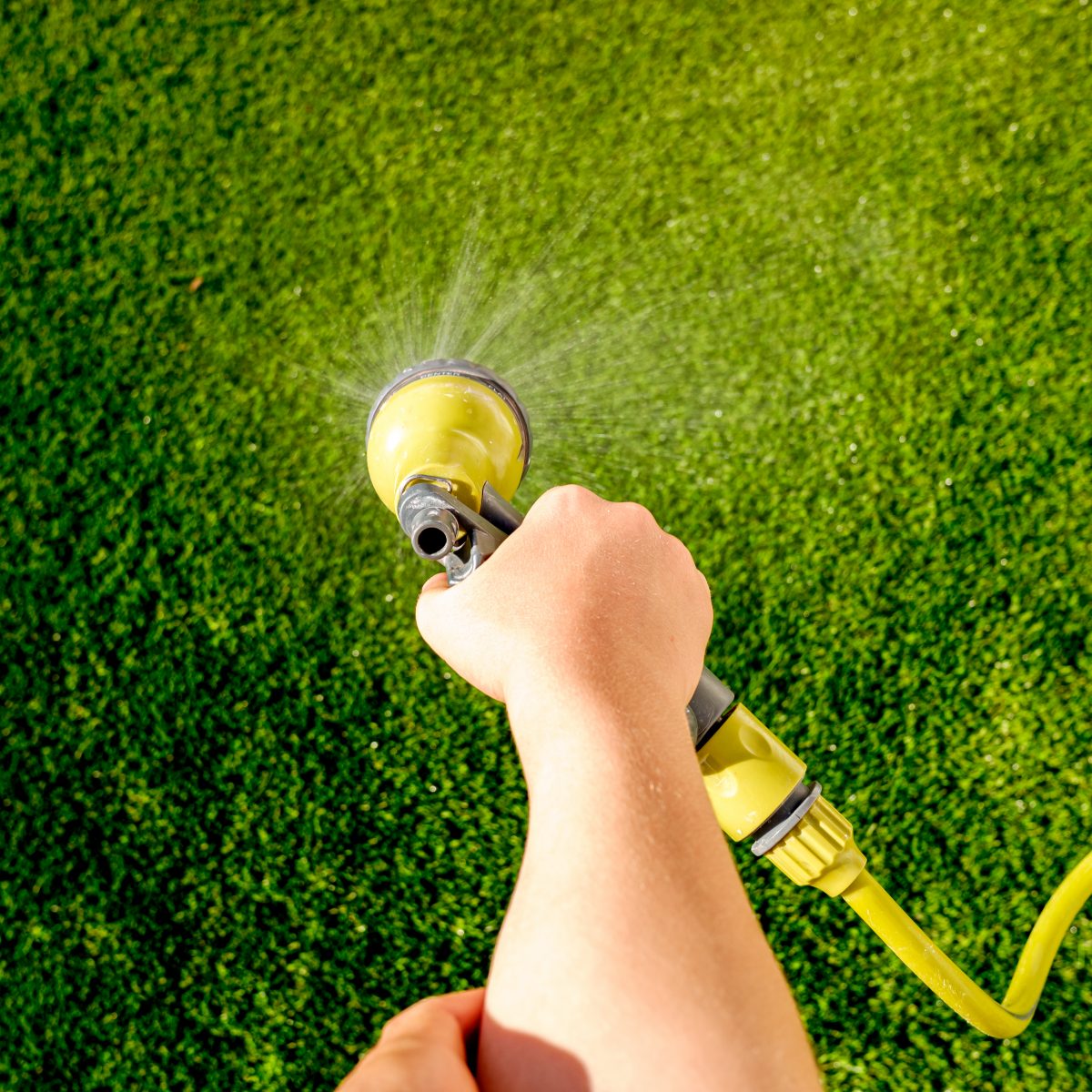 Child's hand watering the grass during the summer with a hose.
